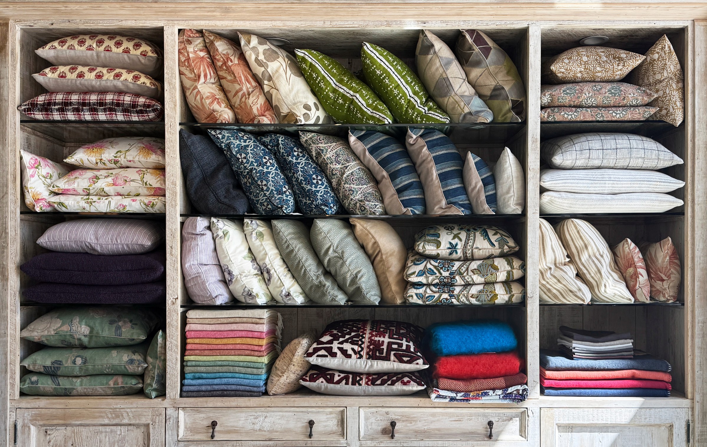 Shelves of decorative pillows at Maude Woods Pasadena featuring vintage textiles, patterned fabrics, and artisanal home décor accents.