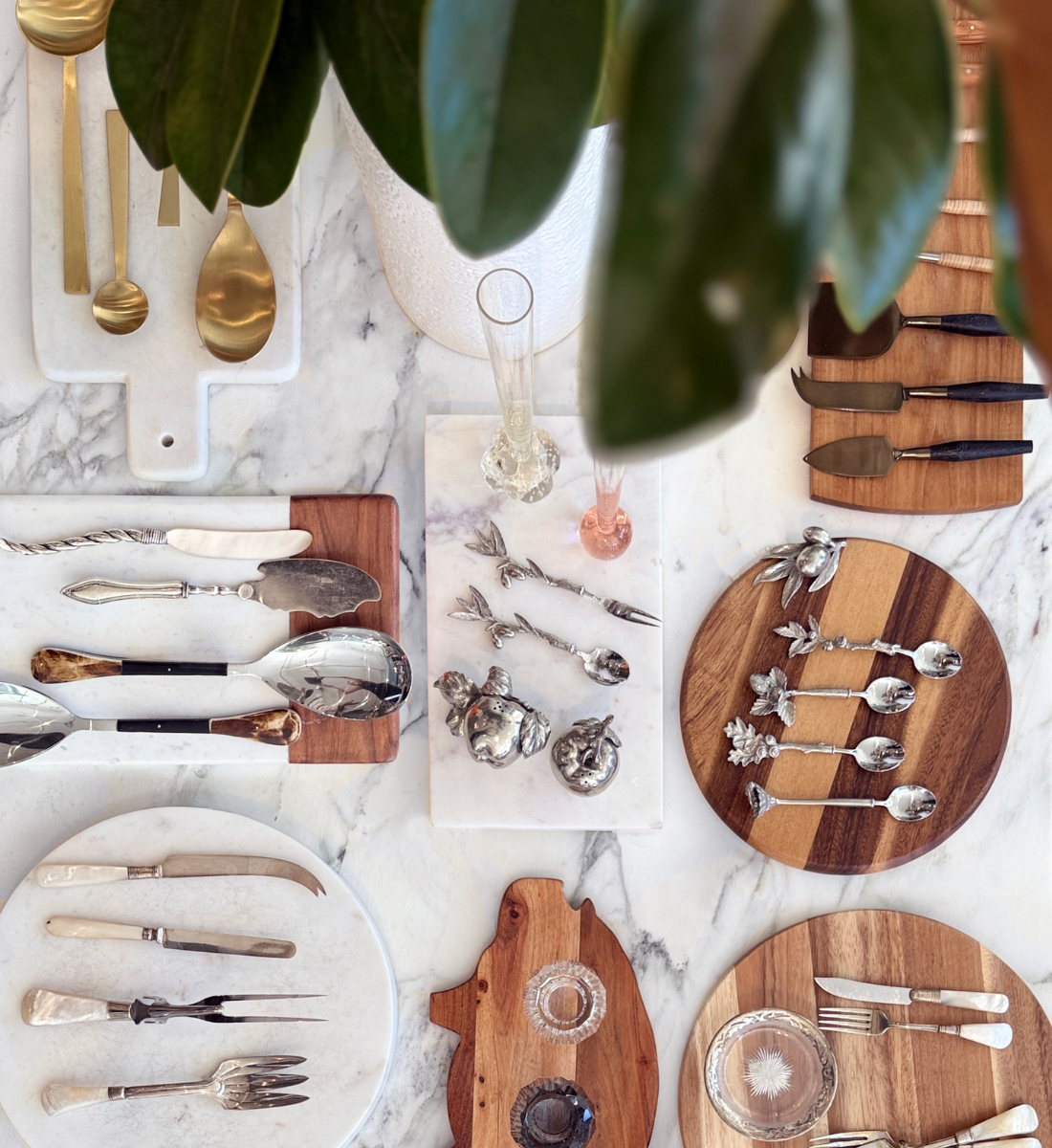 Flat-lay of tabletop décor at Maude Woods Pasadena featuring vintage serving utensils, marble boards, and wood cutting boards arranged on a marble surface.