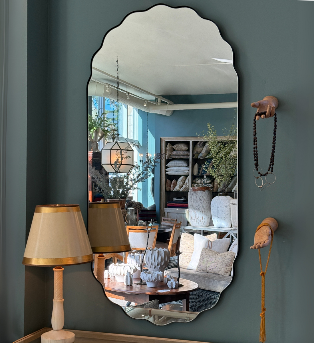 Elegant wall mirror reflecting the interior of Maude Woods Pasadena, surrounded by vintage furniture, lighting, and decorative home accents.
