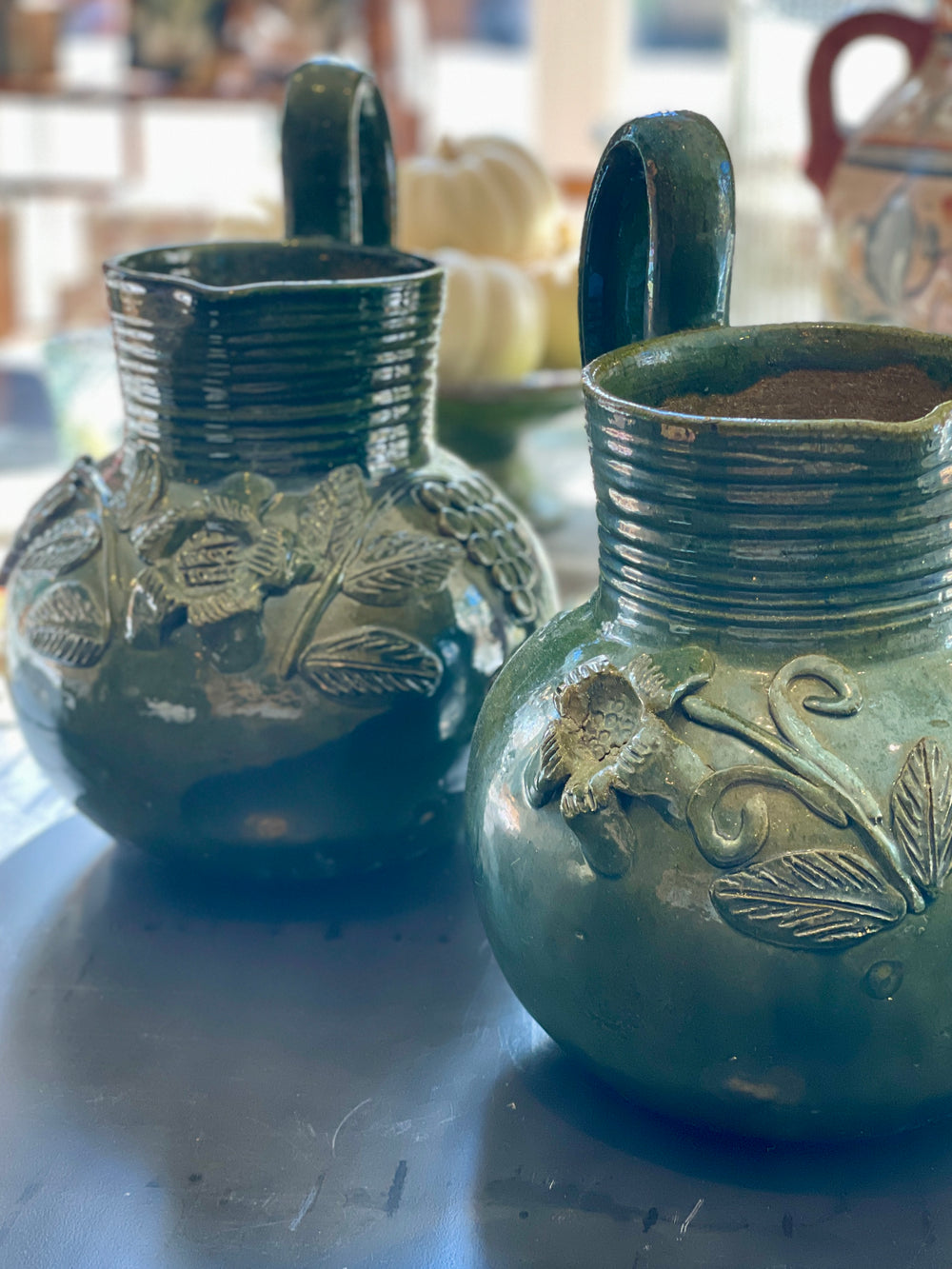 Two green ceramic pitchers with leaf designs on a reflective surface.