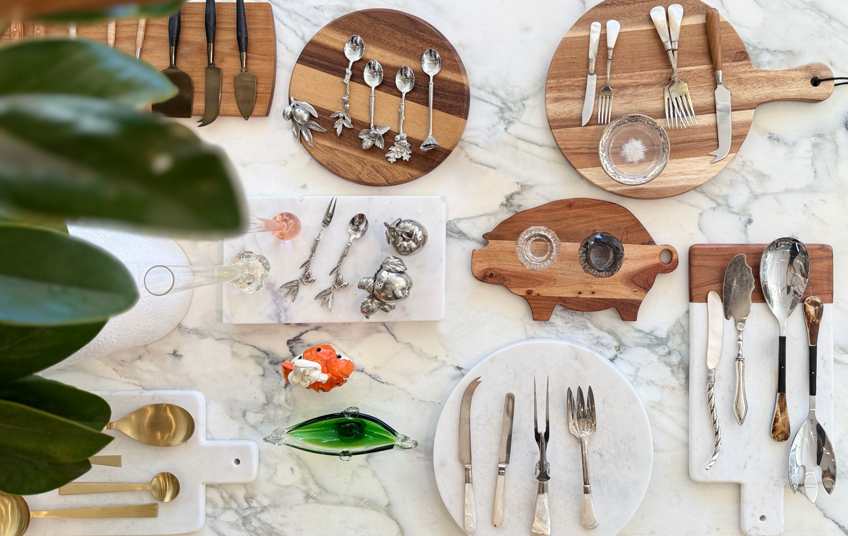 Flat-lay of tabletop décor at Maude Woods Pasadena featuring vintage serving utensils, marble boards, and wood cutting boards arranged on a marble surface.